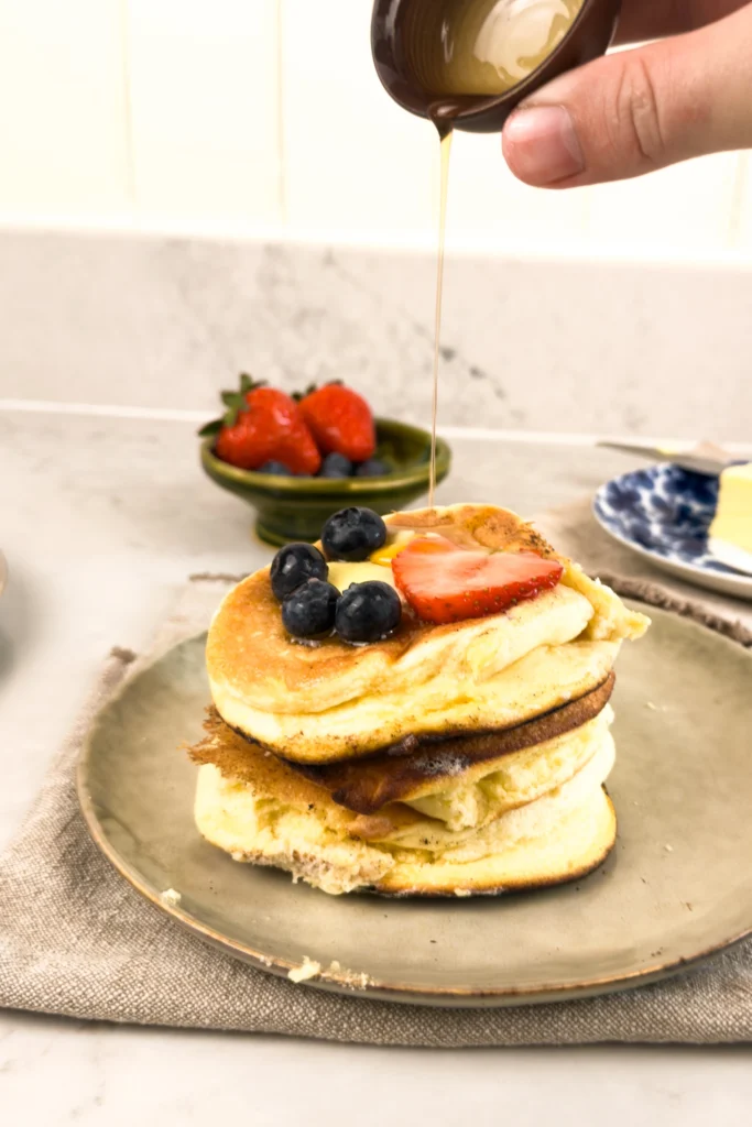 Fluffiga japanska pannkakor - sedd från sidan med lönnsirap ringlad ovanpå - serverad med färska bär