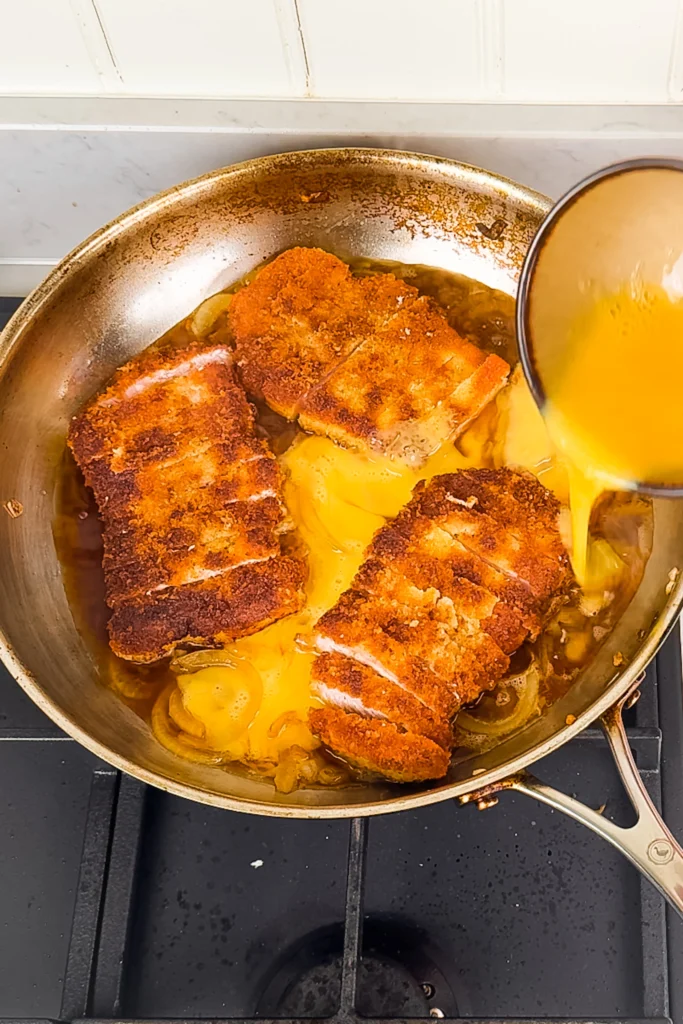 Katsudon instruktioner - steg 5 - ringla ägget över schnitzeln och löksåsen. Låt tillagas tills gulan precis stelnat (det går fort)