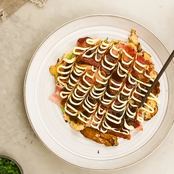 Äkta okonomiyaki - en japansk kålpannkaka serverad "som du vill ha den". Serveras med okonomisås och japansk majonnäs, med valfria tillbehör - sedd ovanifrån